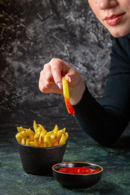 Vooraanzicht heerlijke frietjes met kruiderijen eten krijgen door vrouwelijke donkere ondergrond