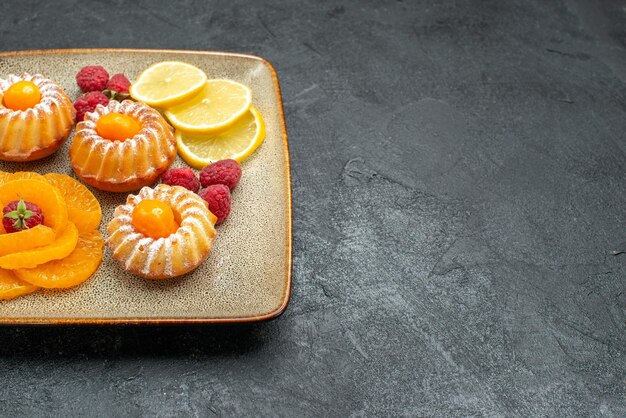 Vooraanzicht heerlijke kleine cakes met schijfjes citroen en mandarijnen op donkere ruimte