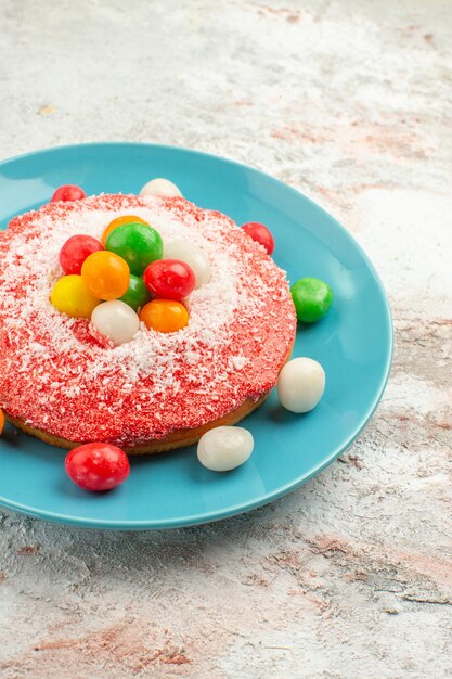 Vooraanzicht heerlijke roze cake met kleurrijke snoepjes in plaat op witte achtergrond taart regenboog kleur cake dessert snoep