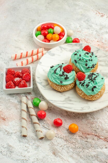 Vooraanzicht heerlijke slagroomtaarten met kleurrijke snoepjes op witte achtergrond dessert thee cake biscuit zoete room