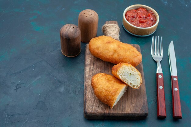 Vooraanzicht heerlijke taarten met vleesvulling en saus op de donkerblauwe oppervlakte van het deegpastei het broodje van het broodbroodje bakken