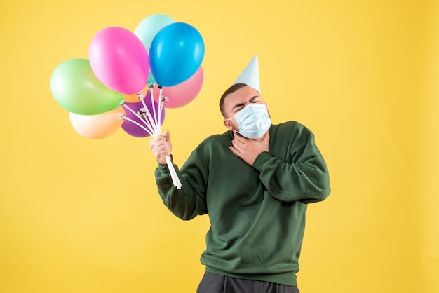 Vooraanzicht jong mannetje dat kleurrijke ballons op geel bureau houdt