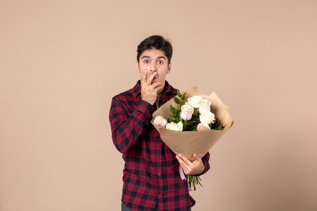 Vooraanzicht jong mannetje dat mooie bloemen op bruine muur houdt