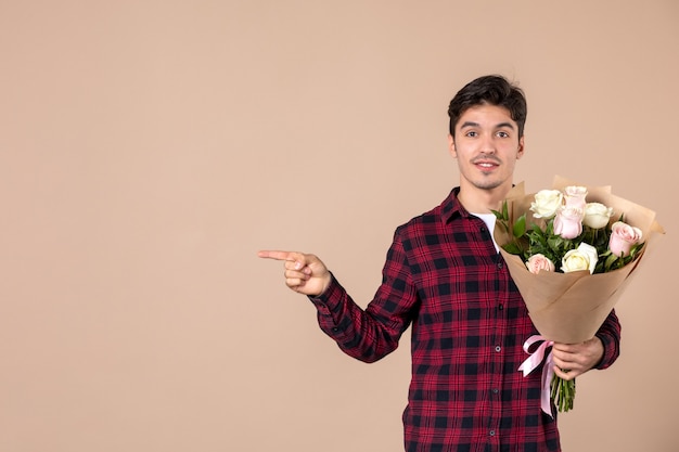 Vooraanzicht jong mannetje dat mooie bloemen op bruine muur houdt