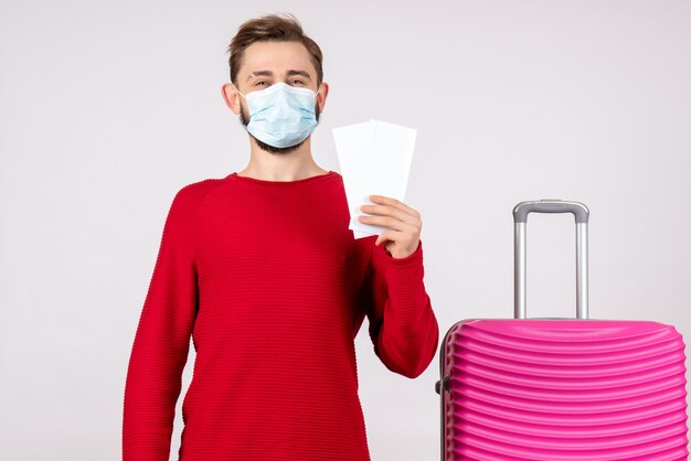 Vooraanzicht jong mannetje in de kaartjes van de maskerholding op de witte emotie van de het viruskleur van de muurreis covid-vlucht