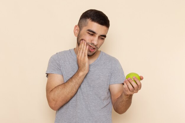 Vooraanzicht jong mannetje in grijs t-shirt met kiespijn die groene appel op beige houdt