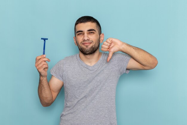 Vooraanzicht jong mannetje in het grijze scheermes van de t-shirtholding en in tegenstelling tot teken op het blauw tonen