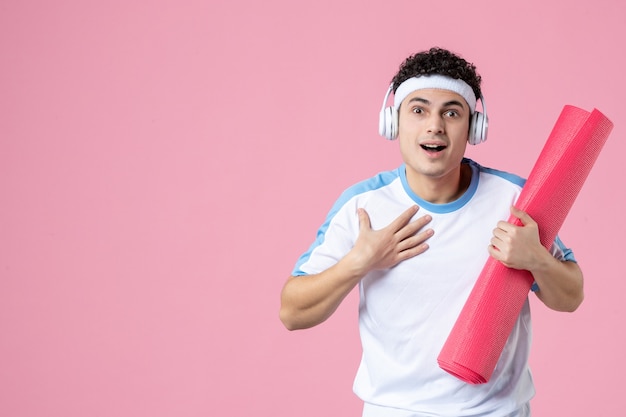 Vooraanzicht jong mannetje in sportkleren met de roze muur van de yogamat