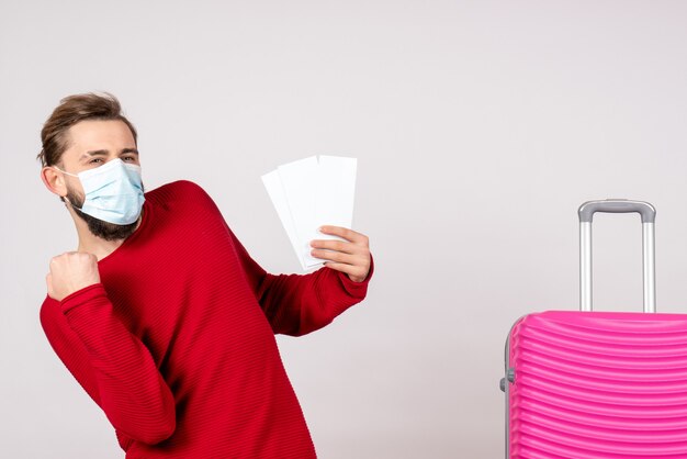 Vooraanzicht jong mannetje in steriel masker met kaartjes op witte muur covid-vliegtuig vakantie emotie vlucht reis kleur