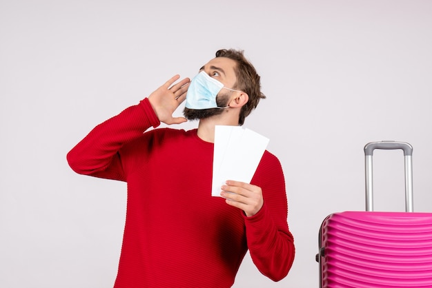 Vooraanzicht jong mannetje in steriel masker met kaartjes op witte muur reis covid-reis vakantie emotie virus vlucht kleur