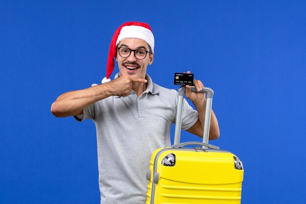 Vooraanzicht jong mannetje met gele zak bankkaart op een blauwe achtergrond reis vakantie emotie