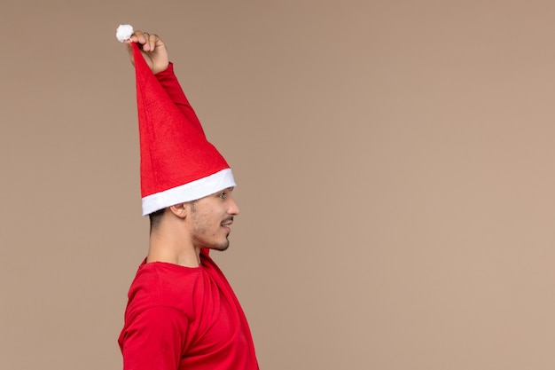 Gratis foto vooraanzicht jong mannetje met kerstmiskaap op bruine kerstmisemotie van de bureauvakantie