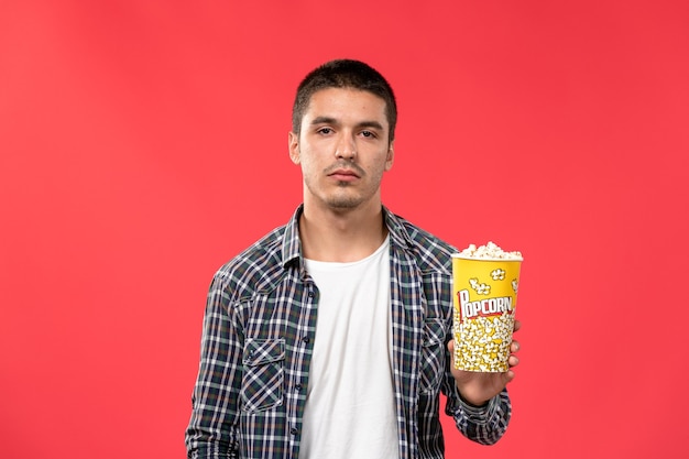 Gratis foto vooraanzicht jong mannetje met popcornpakket op rode muur bioscoop theater filmfilm