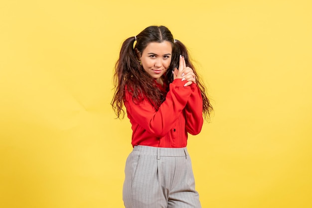 Vooraanzicht jong meisje in rode blouse met pistool met pose op gele achtergrond onschuld kind jeugd kind meisje vrouwelijk