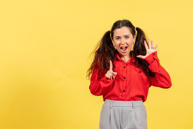 Vooraanzicht jong meisje in rode blouse met schattig haar en grappig gezicht op gele achtergrond onschuld kind meisje jeugd kleur kid