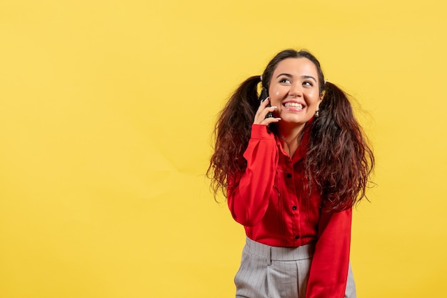 Vooraanzicht jong meisje in rode blouse met schattig haar praten aan de telefoon op gele achtergrond kleur kind meisje kind jeugd onschuld