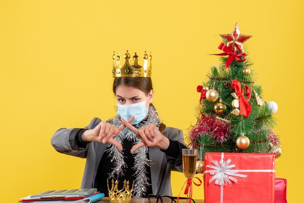 Vooraanzicht jong meisje met medisch masker die kroon kruisen die haar de boom van de vingerskerstmis en giftencocktail kruisen