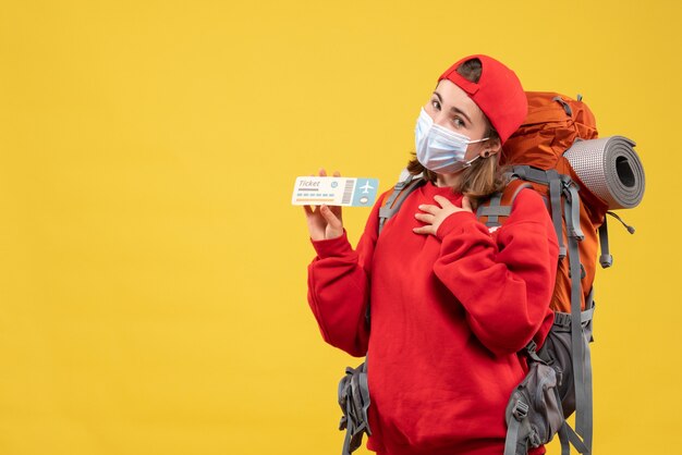 Vooraanzicht jong reizigersmeisje met rugzak en het vliegtuigticket van de maskerholding