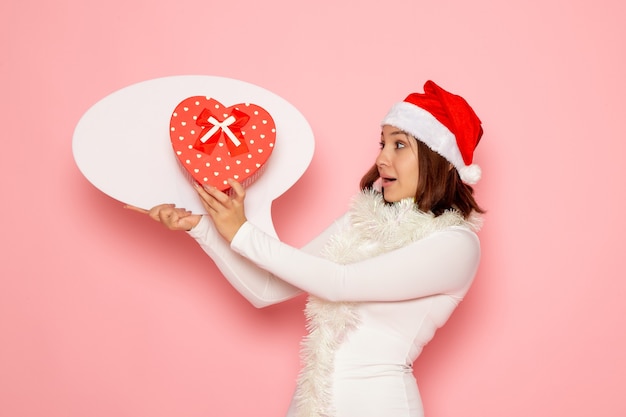 Vooraanzicht jong wijfje dat groot wit teken houdt en op roze muur de vakantie van het kerstmis nieuwe jaar van de emotiekleur houdt