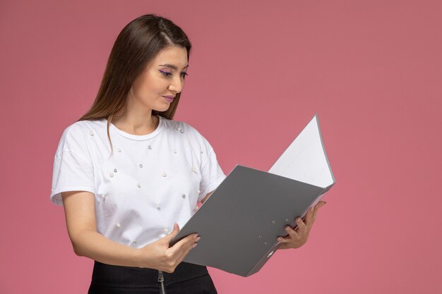 Vooraanzicht jong wijfje dat in wit overhemd grijs dossier op de roze muur, modelvrouw leest