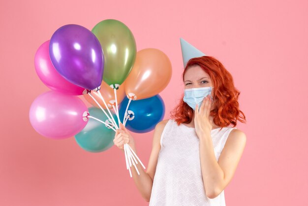 Vooraanzicht jong wijfje dat kleurrijke ballons in masker op roze houdt