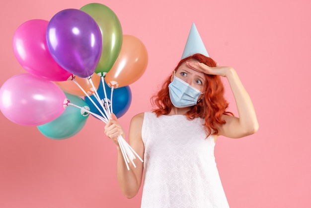 Vooraanzicht jong wijfje dat kleurrijke ballons in masker op roze houdt