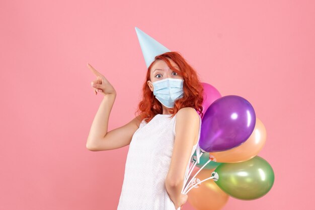 Vooraanzicht jong wijfje dat kleurrijke ballons in steriel masker op de roze achtergrondkleur van partij covid nieuwjaar Kerstmis verbergt