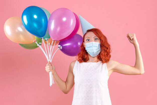 Vooraanzicht jong wijfje dat kleurrijke ballons in steriel masker op roze houdt