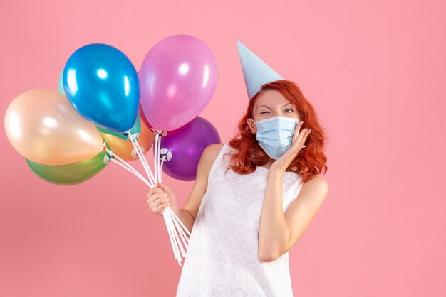 Vooraanzicht jong wijfje dat kleurrijke ballons in steriel masker op roze houdt