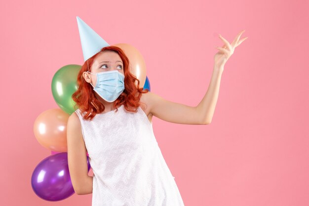 Vooraanzicht jong wijfje dat kleurrijke ballons in steriel masker op roze houdt