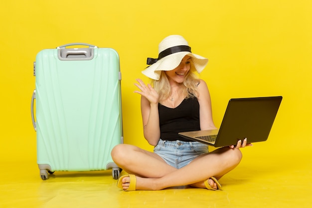 Vooraanzicht jong wijfje die haar laptop op gele muur van de de vakantiereis vrouwelijke zon van de de reisreis met behulp van