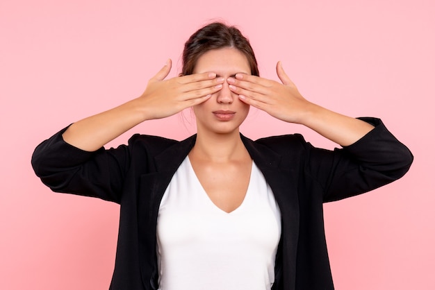 Gratis foto vooraanzicht jong wijfje in donker jasje die haar ogen op roze achtergrond behandelen