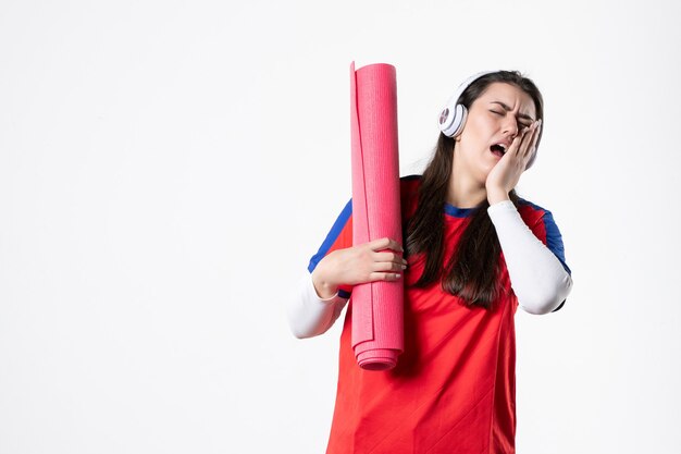 Vooraanzicht jong wijfje in sportkleren die yogamat houden en kiespijn hebben