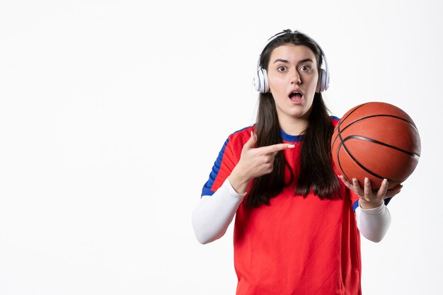 Vooraanzicht jong wijfje in sportkleren met basketbal witte muur