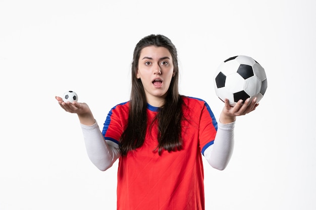 Vooraanzicht jong wijfje in sportkleren met voetbal op witte muur