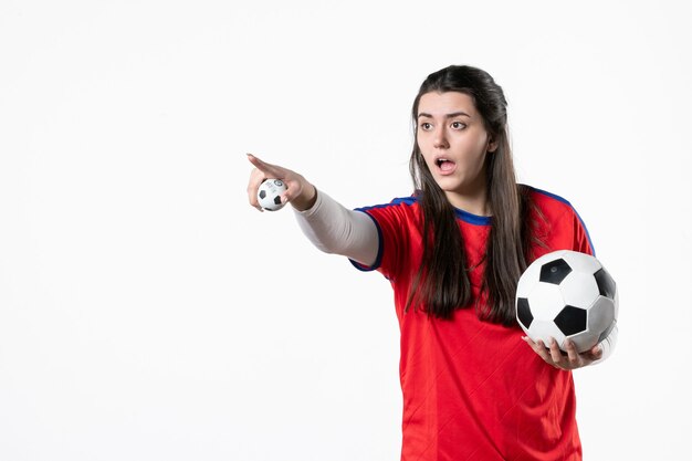 Vooraanzicht jong wijfje in sportkleren met voetbal op witte muur