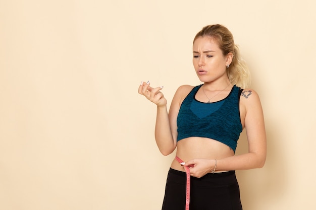 Vooraanzicht jong wijfje in sportuitrusting die haar lichaam op wit de gezondheid van het de schoonheidstraining van de bureausport meten