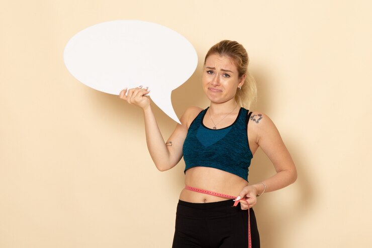Gratis Foto vooraanzicht jong wijfje in sportuitrusting die wit bord houden en haar lichaam op een witte muur meten fit lichaam gezondheid sport schoonheid oefeningen