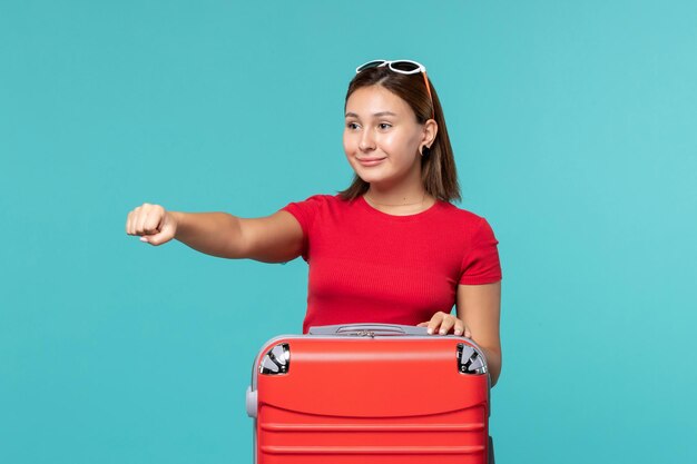 Vooraanzicht jong wijfje met rode zak die zich voor vakantie klaarmaken die op blauwe ruimte glimlachen