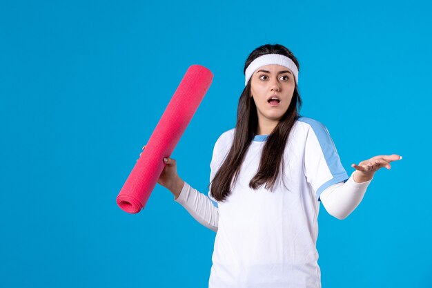 Vooraanzicht jong wijfje met yogamat op blauwe muur