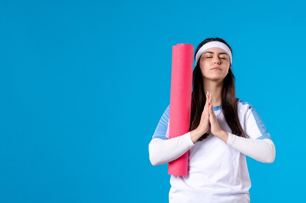 Vooraanzicht jong wijfje met yogamat op blauwe muur