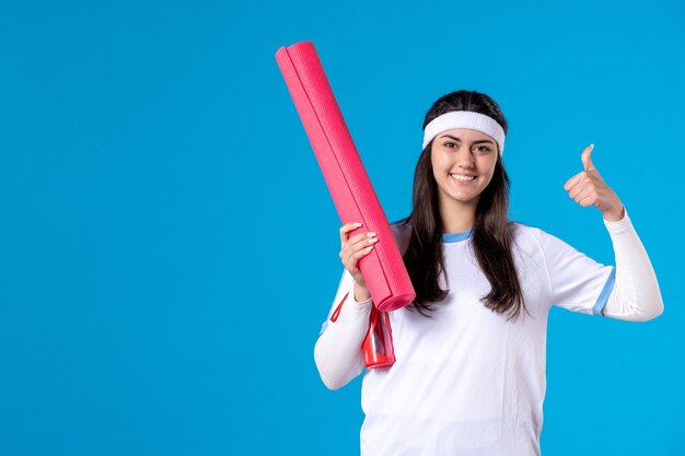 Vooraanzicht jong wijfje met yogamat op blauwe muur