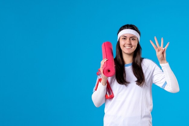 Vooraanzicht jong wijfje met yogamat op blauwe muur