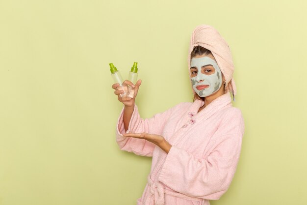 Vooraanzicht jong wijfje na douche in roze de samenstellingsverwijderaars van de badjasholding op groen bureau