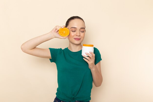 Vooraanzicht jonge aantrekkelijke vrouw in donkergroen shirt met oranje en kan op beige