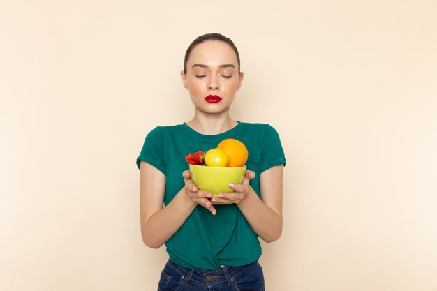 Vooraanzicht jonge aantrekkelijke vrouw in donkergroene shirt met plaat met fruit