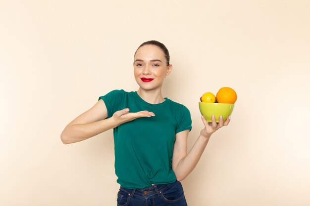 Vooraanzicht jonge aantrekkelijke vrouw in donkergroene shirt met plaat met fruit