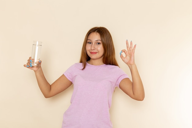 Vooraanzicht jonge aantrekkelijke vrouw in roze t-shirt en spijkerbroek met glas water met glimlach