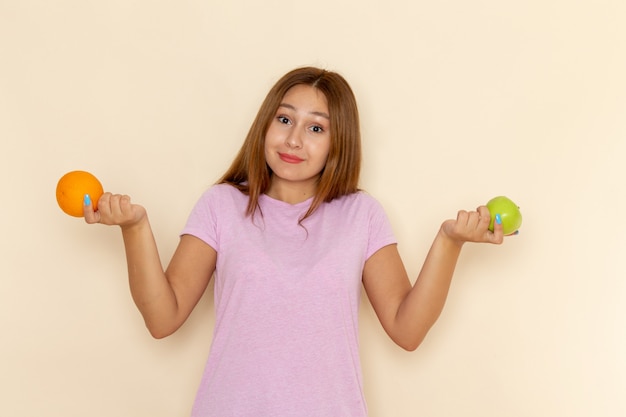 Vooraanzicht jonge aantrekkelijke vrouw in roze t-shirt en spijkerbroek met sinaasappel en appel