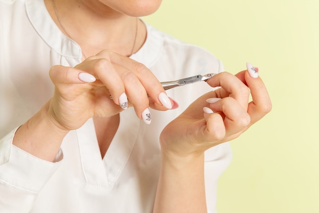 Vooraanzicht jonge aantrekkelijke vrouw in wit overhemd tot vaststelling van haar nagels op het groene oppervlak